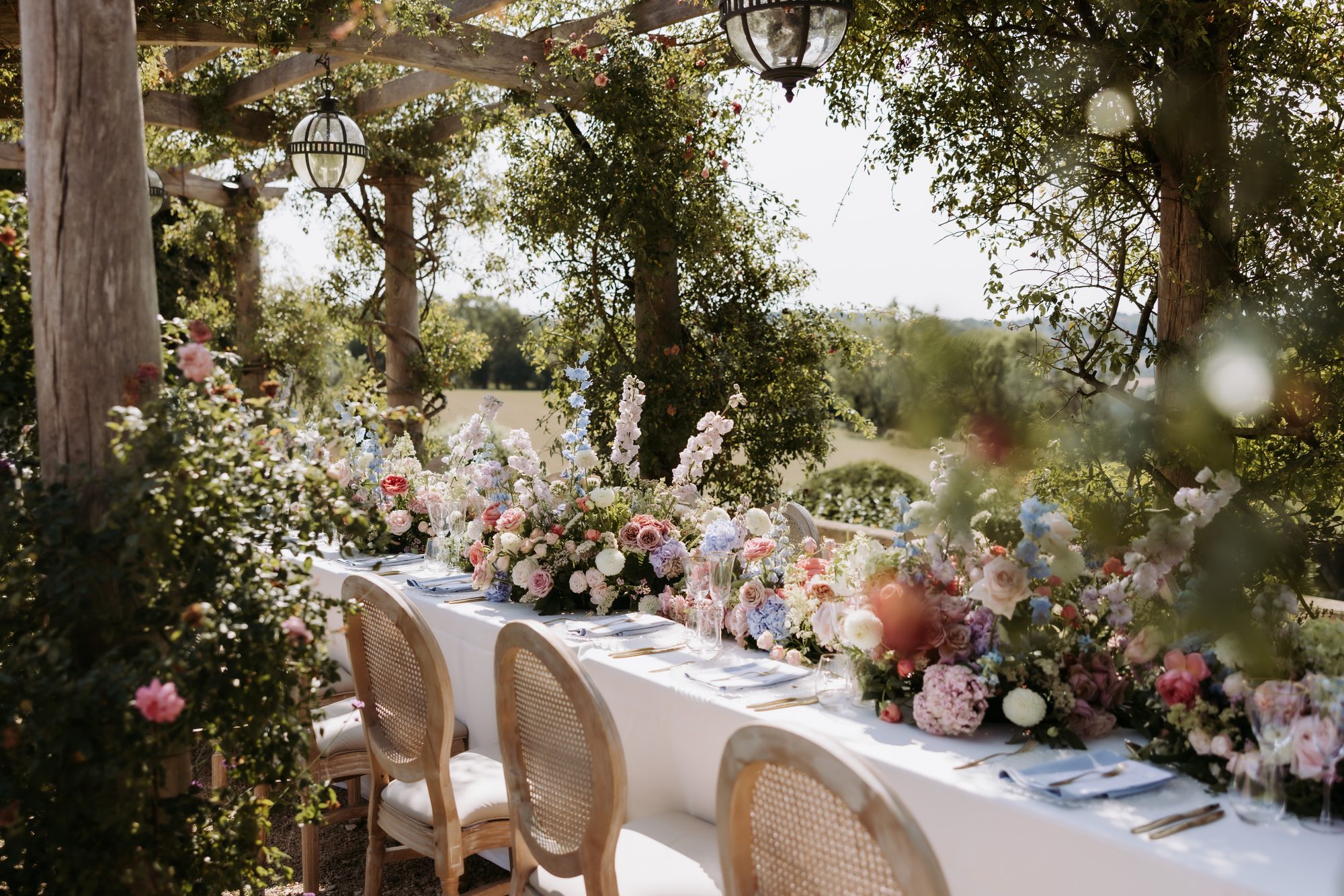 Long pergola dining table set for a wedding, dressed with abundant florals